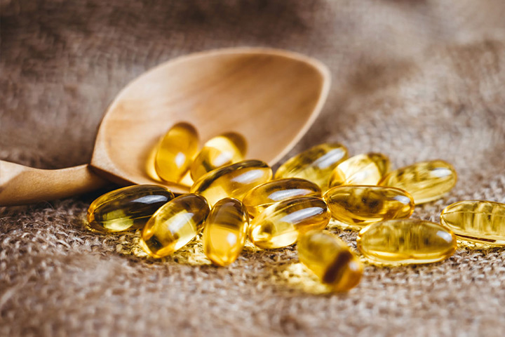 Natural Pharmaceuticals CalciumControl™ Kollased kalaõli kapslid puidust lusikal, asetatud linasele riidele tervise toetamiseks.